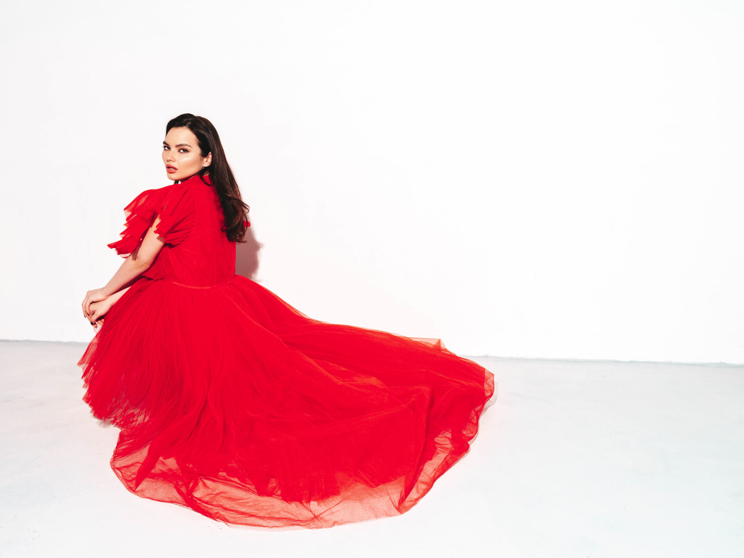 High fashion portrait of young beautiful brunette woman wearing nice trendy red evening fluffy dress. Sexy fashion model posing in studio. Fashionable female isolated